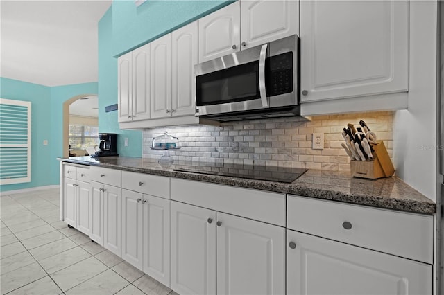 kitchen featuring tasteful backsplash, stainless steel microwave, dark stone counters, arched walkways, and white cabinetry