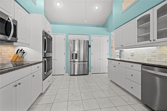 kitchen with dark stone counters, stainless steel appliances, decorative backsplash, white cabinets, and glass insert cabinets