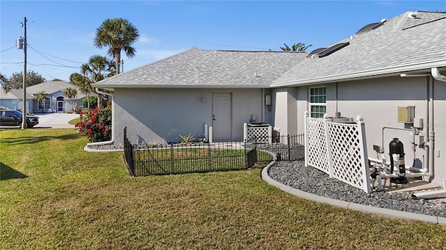 exterior space with stucco siding, fence, a lawn, and a shingled roof