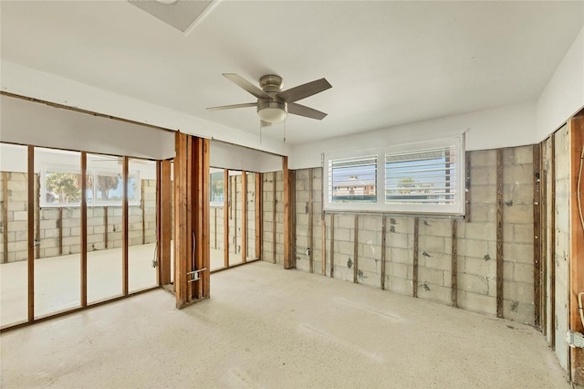 empty room featuring a healthy amount of sunlight, a ceiling fan, and concrete block wall