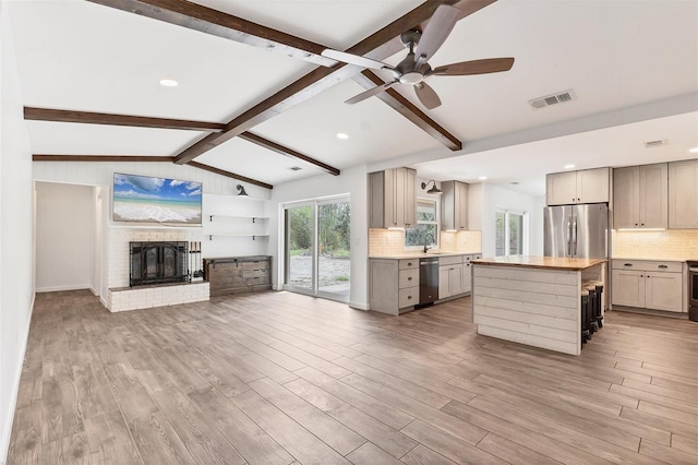 kitchen featuring stainless steel appliances, lofted ceiling with beams, light wood-style floors, open floor plan, and a sink