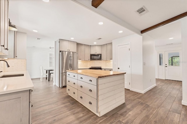 kitchen featuring beam ceiling, stainless steel appliances, visible vents, wooden counters, and a sink