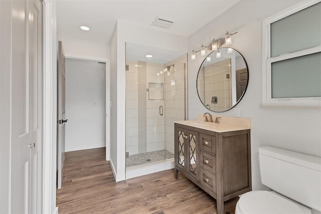 bathroom with a stall shower, visible vents, toilet, wood finished floors, and vanity