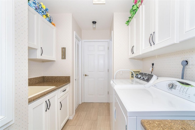 laundry area featuring a sink, washing machine and clothes dryer, cabinet space, and wallpapered walls