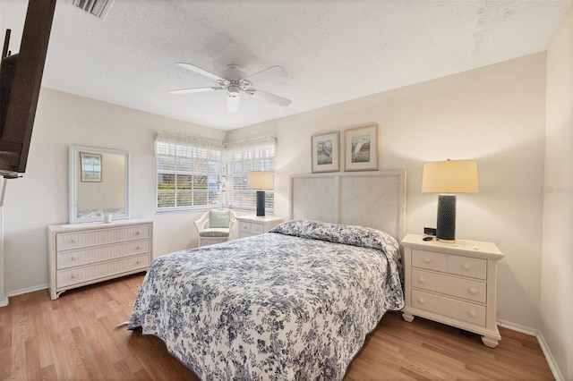 bedroom featuring light wood-style floors, baseboards, visible vents, and a textured ceiling