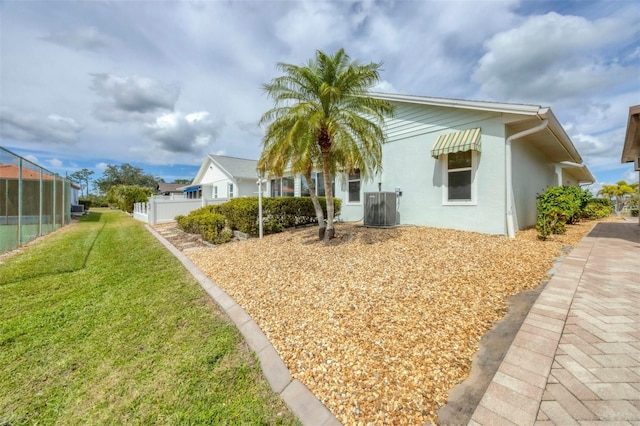 exterior space with central air condition unit, stucco siding, fence, and a front yard