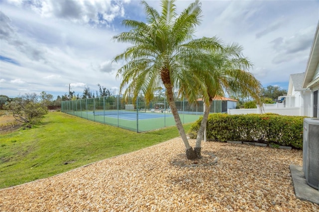 view of tennis court with a yard and fence