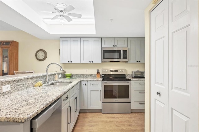 kitchen with a peninsula, a sink, appliances with stainless steel finishes, a raised ceiling, and light wood-type flooring