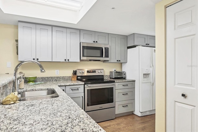 kitchen with a toaster, gray cabinets, light wood-style flooring, stainless steel appliances, and a sink