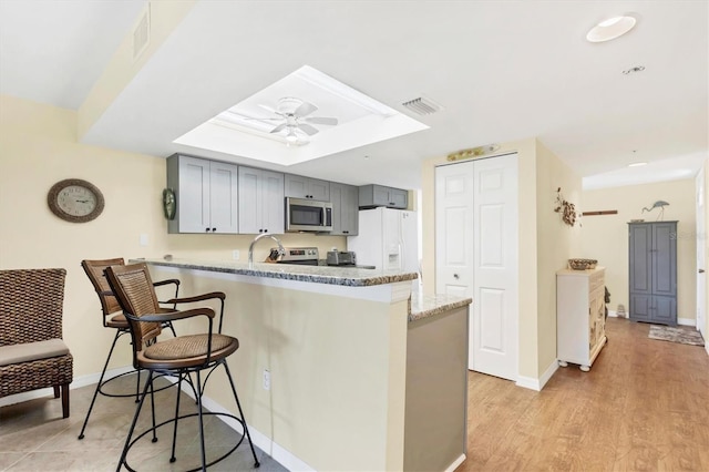 kitchen with visible vents, a peninsula, ceiling fan, stainless steel microwave, and a kitchen breakfast bar