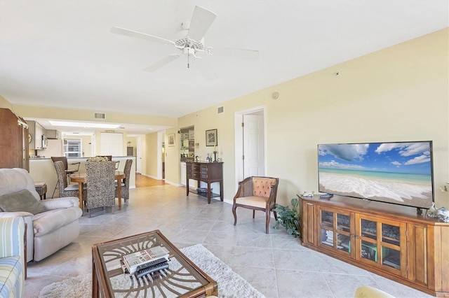 living area featuring light tile patterned floors, baseboards, visible vents, and ceiling fan