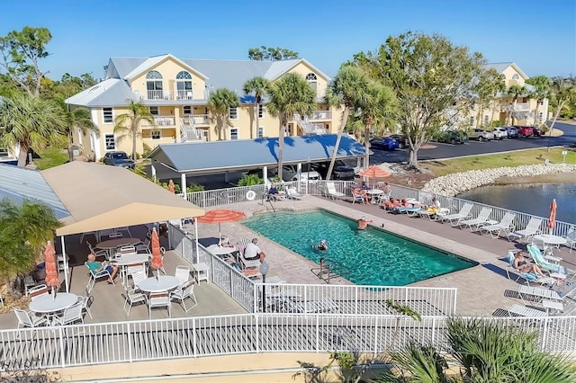 community pool with a water view, fence, and a patio area