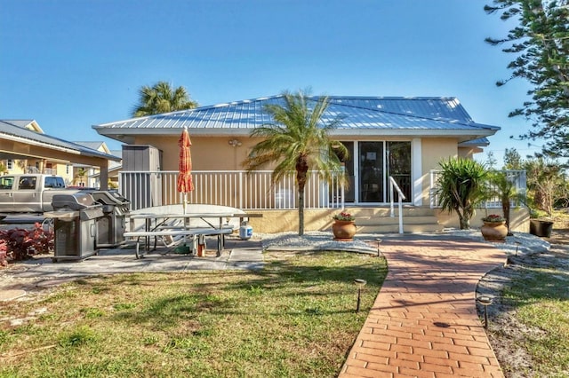 back of house featuring stucco siding, a patio, metal roof, and a lawn