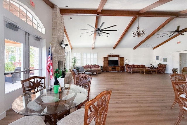 dining area with high vaulted ceiling, wood finished floors, a stone fireplace, and ceiling fan with notable chandelier