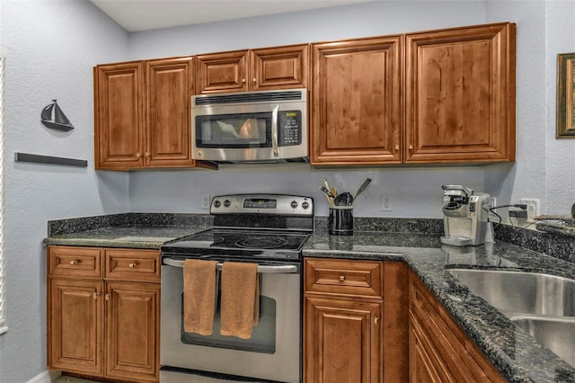 kitchen featuring dark stone counters, stainless steel appliances, a sink, and brown cabinets