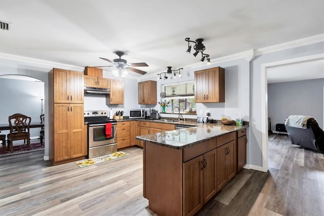 kitchen featuring arched walkways, under cabinet range hood, stainless steel appliances, a peninsula, and dark stone counters