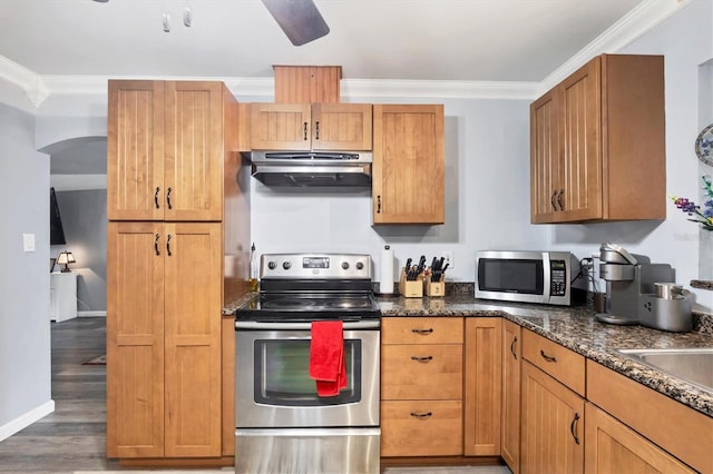 kitchen featuring arched walkways, light wood-style floors, appliances with stainless steel finishes, ornamental molding, and under cabinet range hood