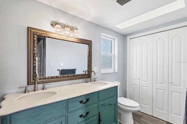 full bathroom with wood finished floors, a sink, toilet, and double vanity