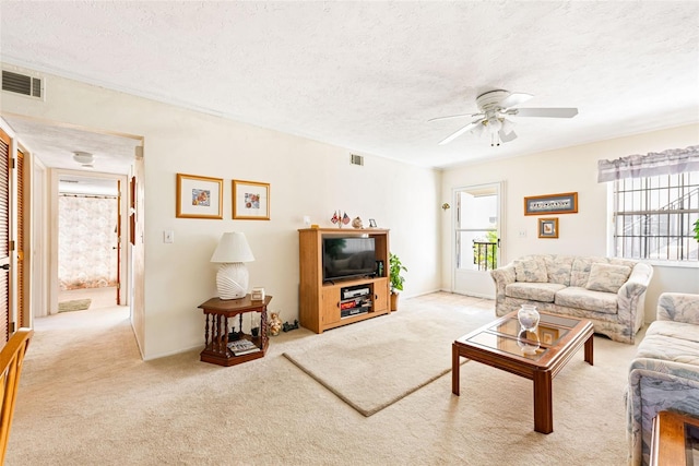 living area with a textured ceiling, ceiling fan, light carpet, and visible vents