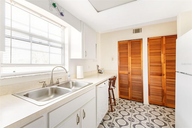 kitchen with light countertops, visible vents, white cabinetry, a sink, and white appliances