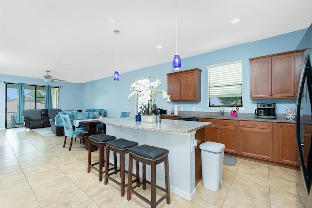 kitchen featuring light tile patterned floors, light stone counters, a breakfast bar area, a sink, and a center island