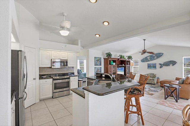 kitchen featuring light tile patterned floors, dark countertops, a breakfast bar area, stainless steel appliances, and a sink