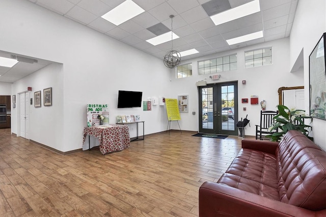 interior space featuring french doors, light wood finished floors, a paneled ceiling, a towering ceiling, and baseboards