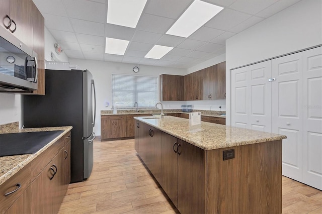 kitchen with stainless steel appliances, light wood-style flooring, a paneled ceiling, and a center island with sink