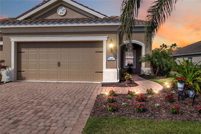 view of front of home featuring an attached garage, a tiled roof, decorative driveway, and stucco siding