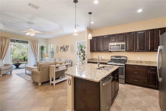 kitchen with a tray ceiling, appliances with stainless steel finishes, open floor plan, and a sink