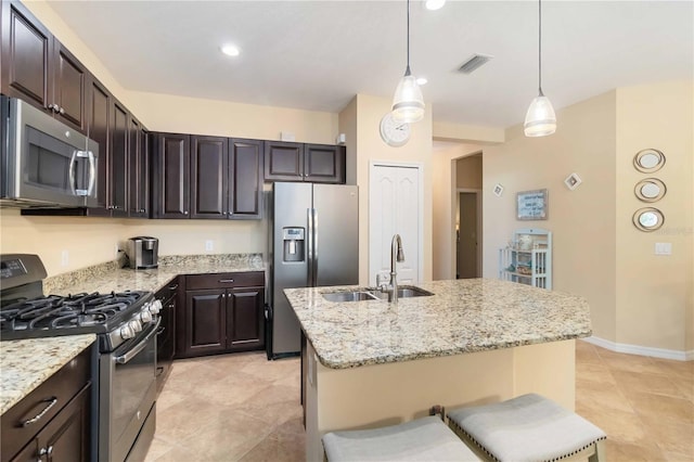 kitchen with a sink, visible vents, appliances with stainless steel finishes, light stone countertops, and a center island with sink