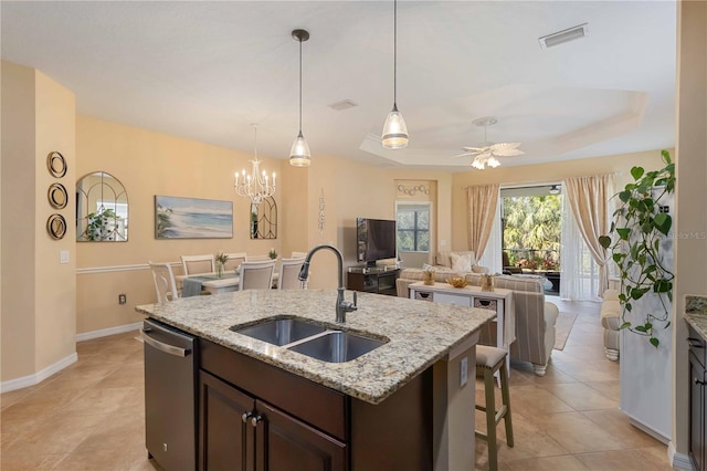 kitchen featuring dark brown cabinetry, dishwasher, an island with sink, a tray ceiling, and a sink