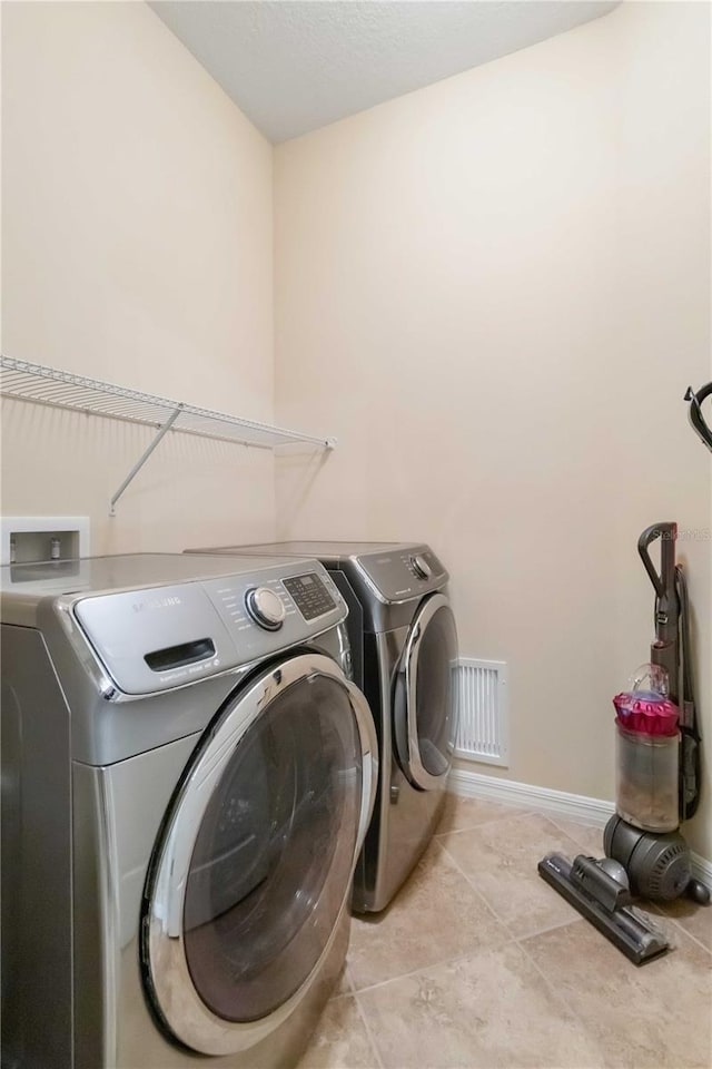 clothes washing area with laundry area, light tile patterned floors, baseboards, visible vents, and washer and dryer