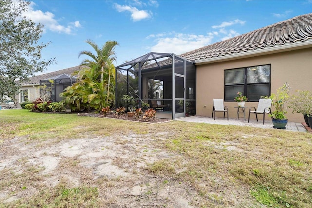 rear view of property featuring a lawn, glass enclosure, a tiled roof, a patio area, and stucco siding