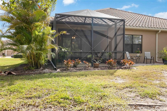 back of house featuring a tile roof, a yard, a patio, stucco siding, and a lanai