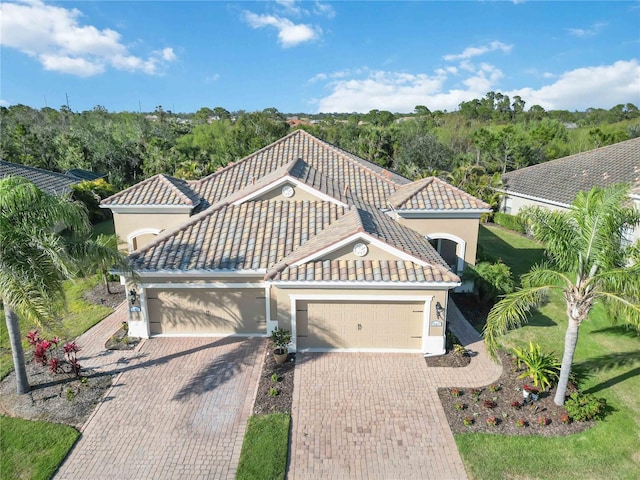 mediterranean / spanish-style house featuring a garage, decorative driveway, a tile roof, and stucco siding