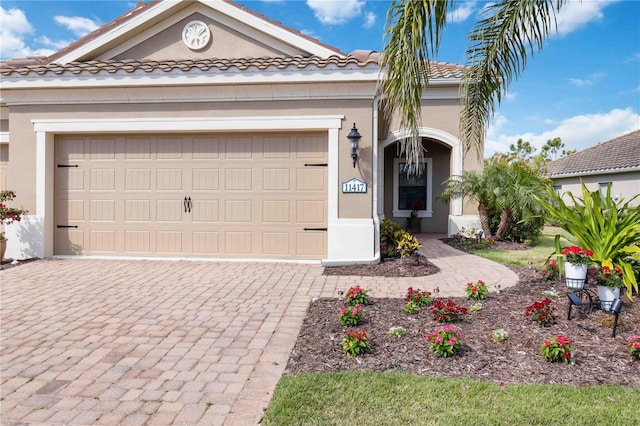 view of front facade featuring a garage, a tiled roof, decorative driveway, and stucco siding