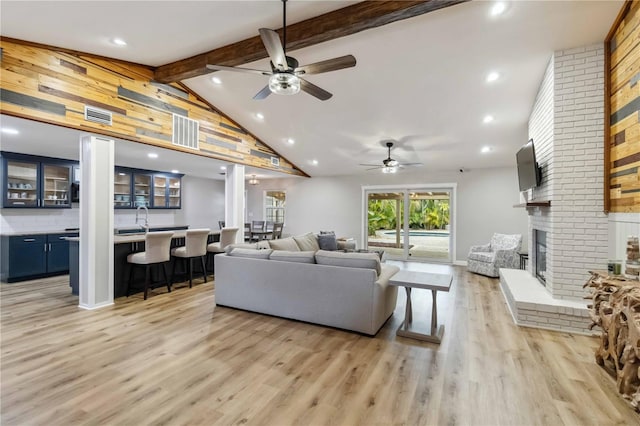 living area featuring visible vents, light wood-style flooring, a brick fireplace, beam ceiling, and recessed lighting