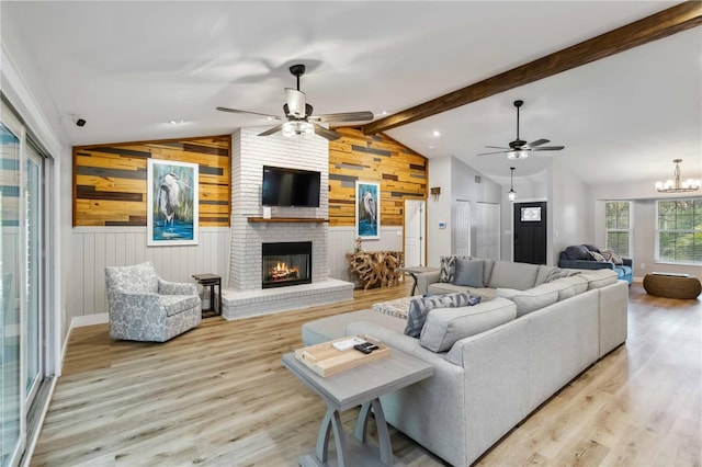 living room with light wood-style floors, a fireplace, lofted ceiling with beams, and ceiling fan with notable chandelier