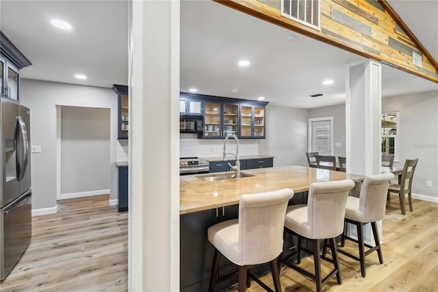 kitchen with appliances with stainless steel finishes, light wood-type flooring, a sink, and butcher block counters