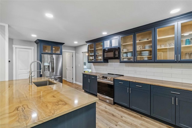 kitchen featuring glass insert cabinets, light wood-style floors, tasteful backsplash, and appliances with stainless steel finishes