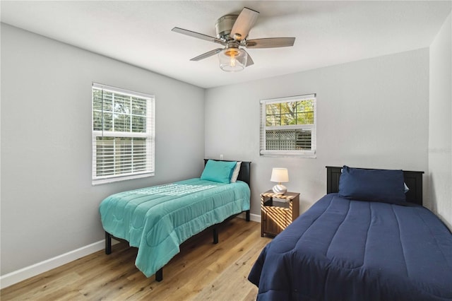 bedroom with baseboards, multiple windows, ceiling fan, and light wood finished floors