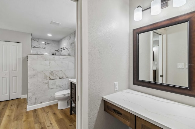 full bathroom with a marble finish shower, a textured wall, toilet, wood finished floors, and vanity