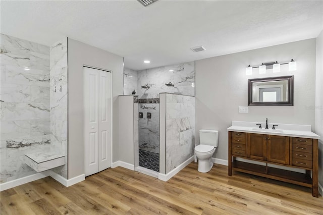 bathroom with a marble finish shower, visible vents, toilet, wood finished floors, and vanity