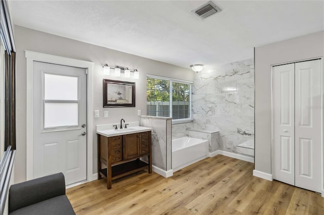 full bath featuring a garden tub, wood finished floors, vanity, visible vents, and baseboards