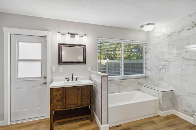 bathroom with a garden tub, wood finished floors, and vanity