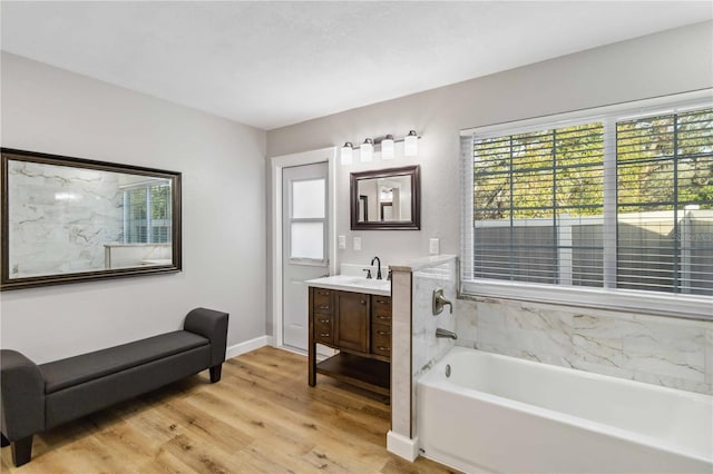 full bathroom featuring a tub to relax in, wood finished floors, vanity, and baseboards