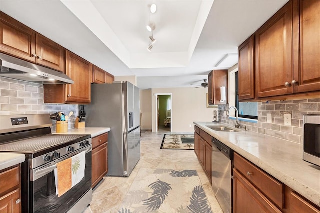 kitchen with under cabinet range hood, a sink, appliances with stainless steel finishes, decorative backsplash, and a tray ceiling