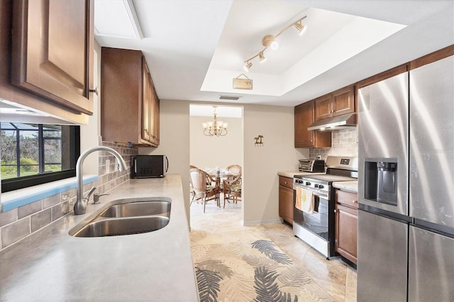 kitchen featuring under cabinet range hood, stainless steel appliances, a sink, light countertops, and a raised ceiling