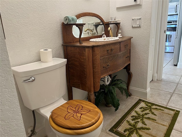 bathroom featuring toilet, tile patterned flooring, a textured wall, and vanity